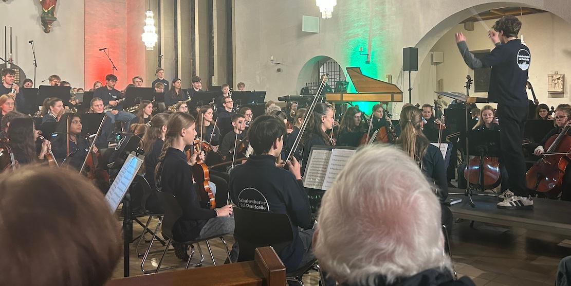 Schüler dirigiert Orchester aus Jugendlichen und Erwachsene in einer Kirche