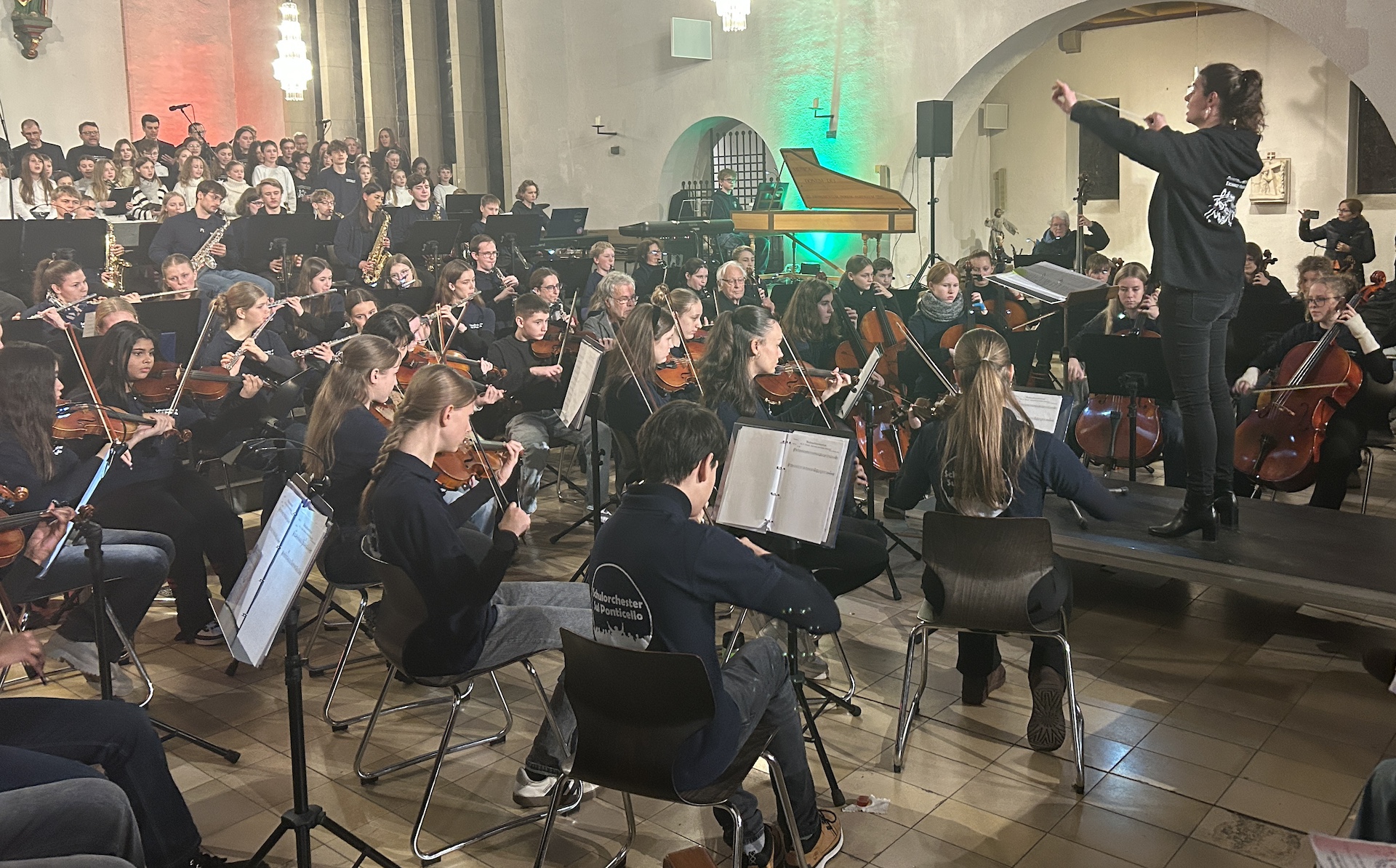 Frau dirigiert Orchester und Chor aus Jugendlichen und Erwachsenen in der Kirche