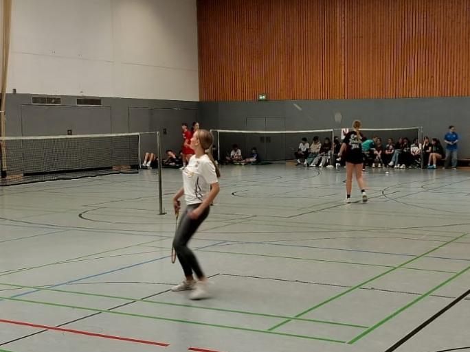 Mädchen und Jungen spielen Badminton in großer Sporthalle