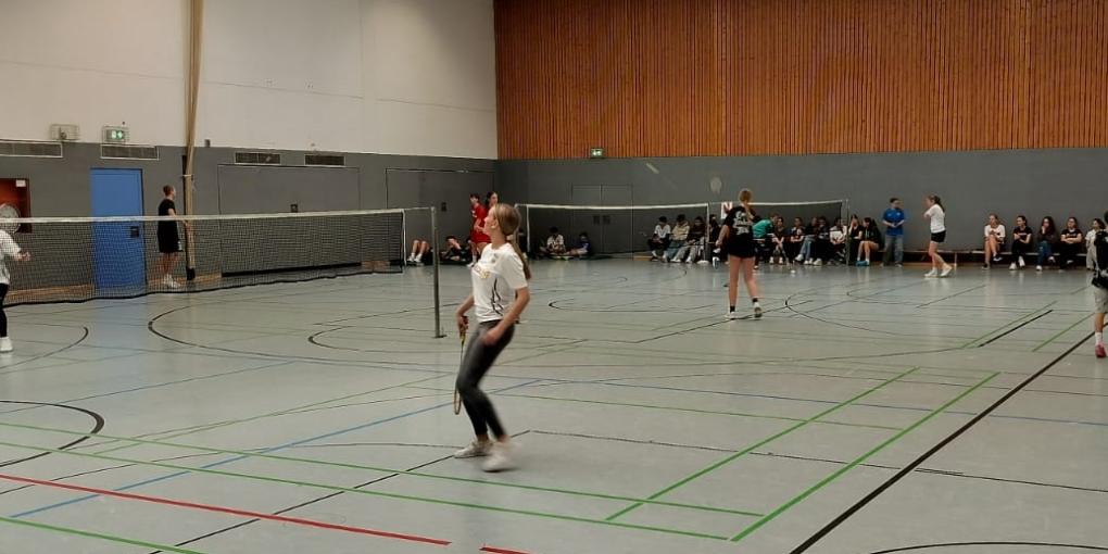 Mädchen und Jungen spielen Badminton in großer Sporthalle