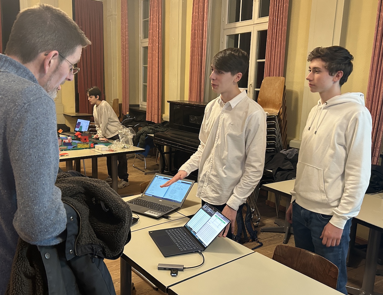 2 Jungen, vor ihnen zwei Notebooks, im Gespräch mit einem Mann