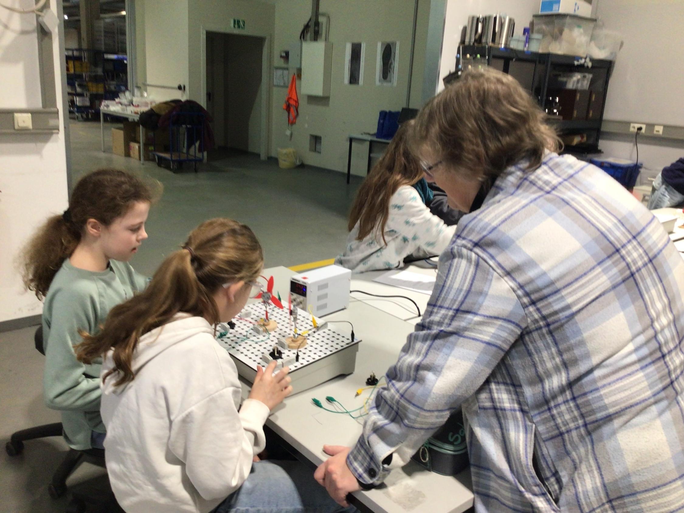 zwei Schülerinnen löten, eine Frau stehen neben ihnen