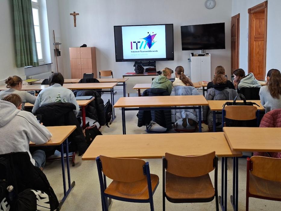 Schüler:innen von hinten in einem Klassenraum, digitales Board mit Schriftzug 'Internet Team Wettbewerb'