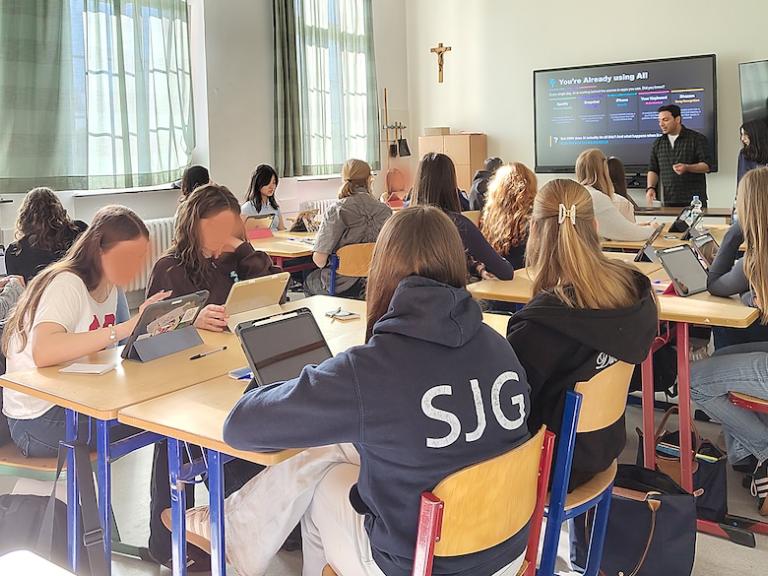 Schülerinnen in einem Klassenraum, Mann vor digitaler Tafel