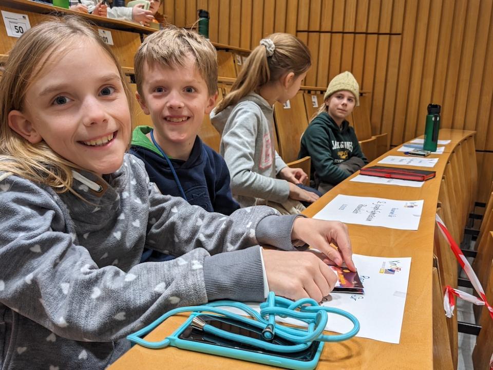 Vier Kinder sitzen in einem Uni-Hörsaal