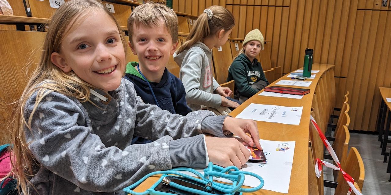 Vier Kinder sitzen in einem Uni-Hörsaal