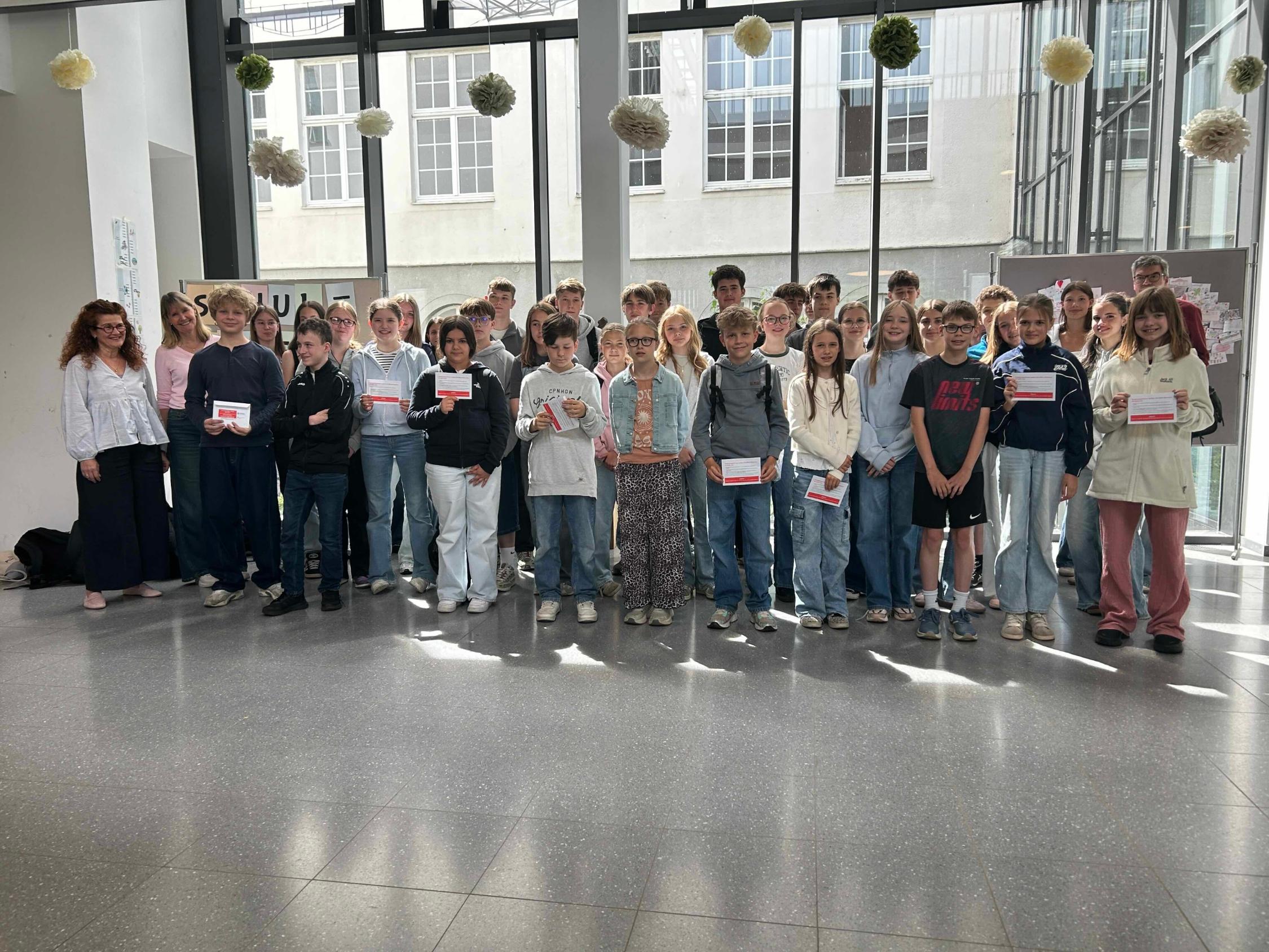 Gruppenbild mit Mädchen und Jungen, die Umschläge in den Händen halten, im Foyer der Schule