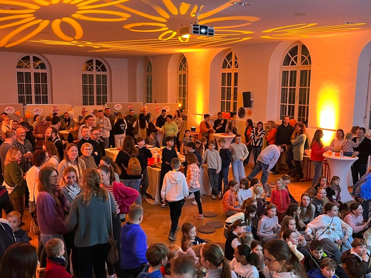 Kinder und Erwachsene stehen mit Blick auf eine digitale Tafel im orange beleuchteten Raum