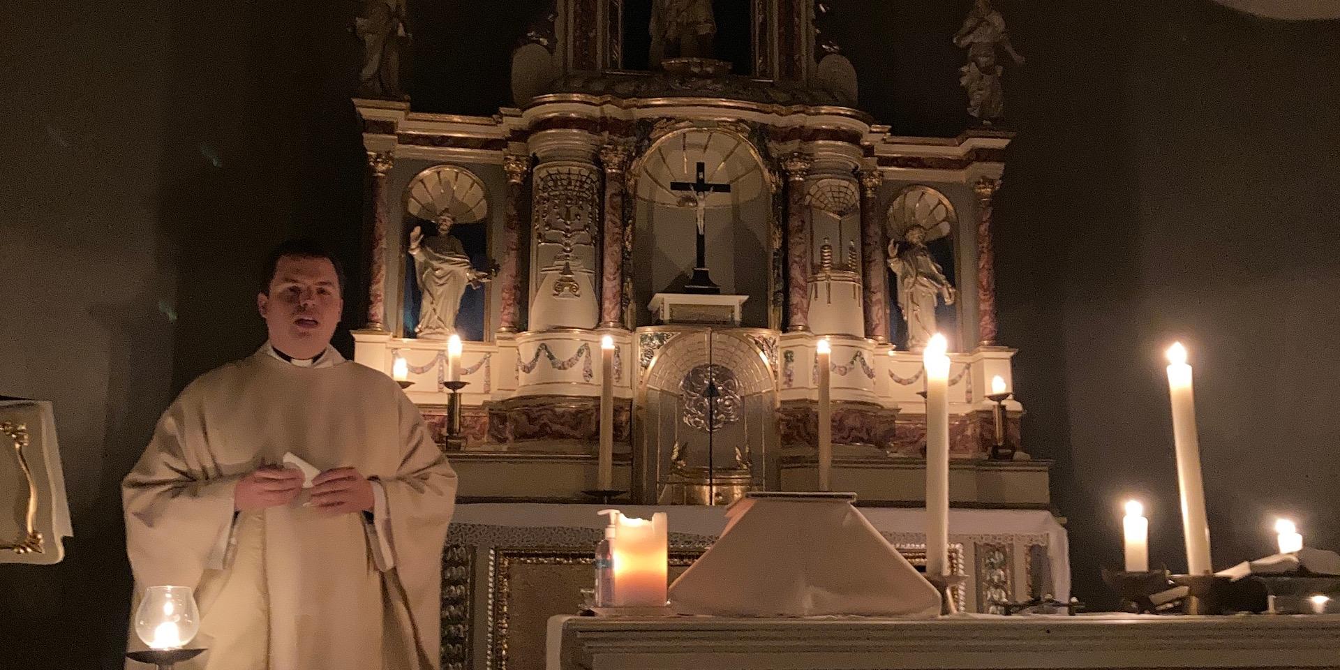 Priester vor mit Kerzen erleuchtetem Altar