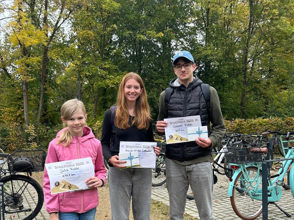 ein Kind, eine Jugendliche, ein Jugendlicher mit Urkunden in der Hand, daneben Fahrräder