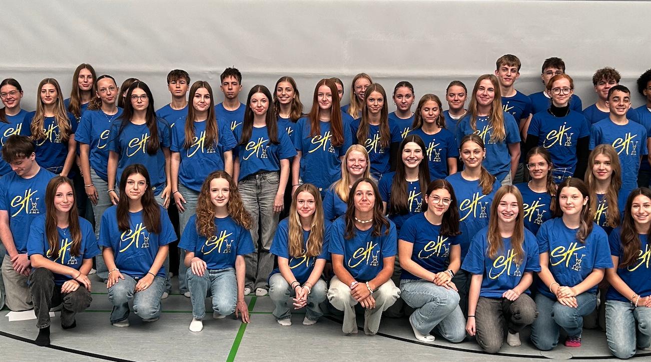 Mädchen und Jungen mit T-Shirt mit Aufdruck 'Sporthelfer' in der Turnhalle