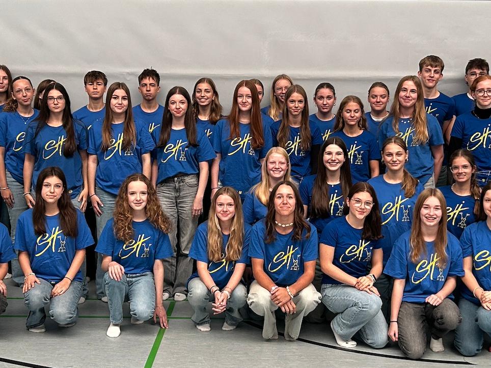 Mädchen und Jungen mit T-Shirt mit Aufdruck 'Sporthelfer' in der Turnhalle