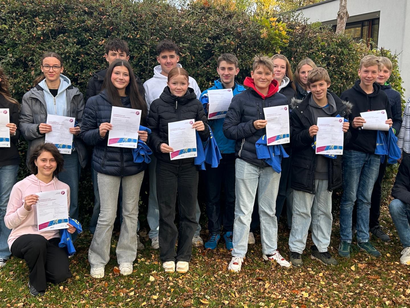Schülerinnen und Schüler, Urkunden und blaue Shirts  in der Hand, Lehrerin am Rand