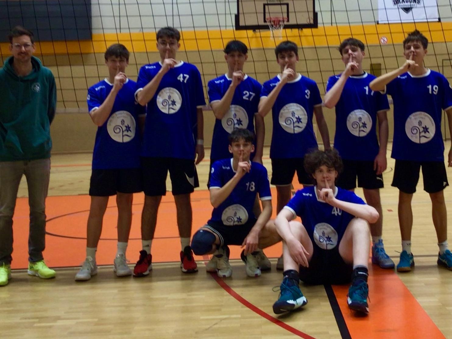 Mannschaftsfoto von Jungen in der Sporthalle vor Volleyballnetz mit Lehrer an der Seite