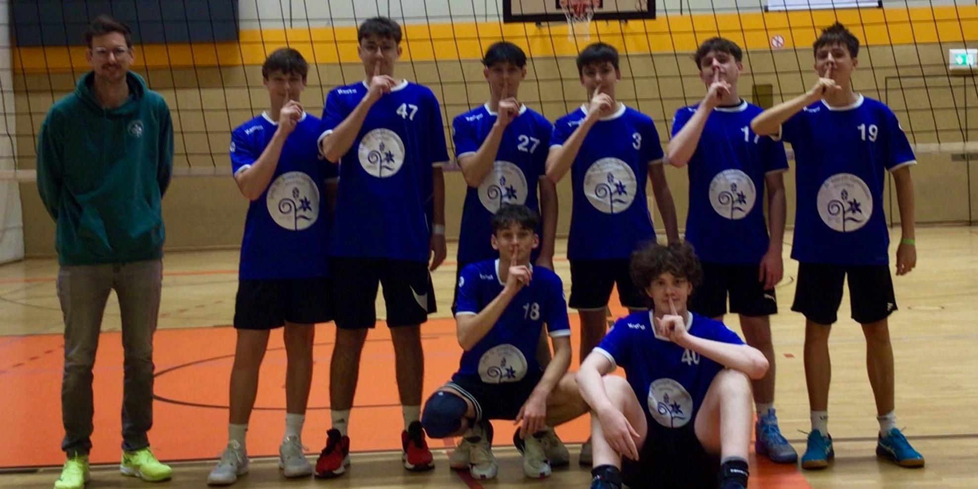 Mannschaftsfoto von Jungen in der Sporthalle vor Volleyballnetz mit Lehrer an der Seite