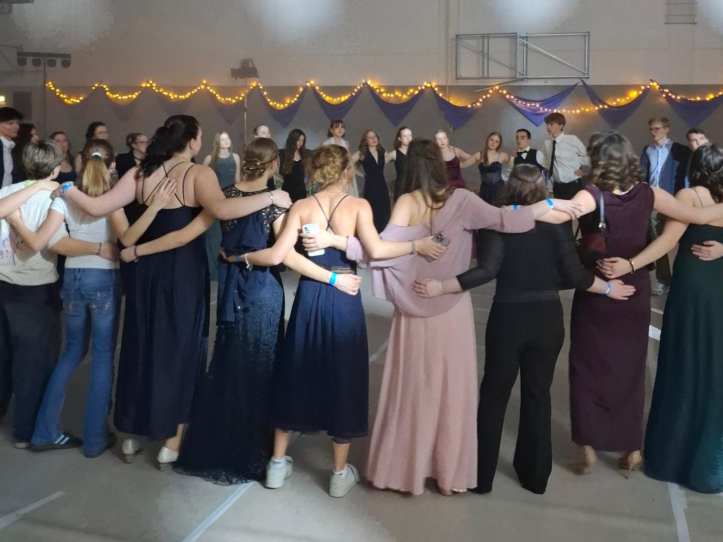 Schülerinnen und Schüler in Ballkleidern und Anzügen stehen umarmend im Kreis